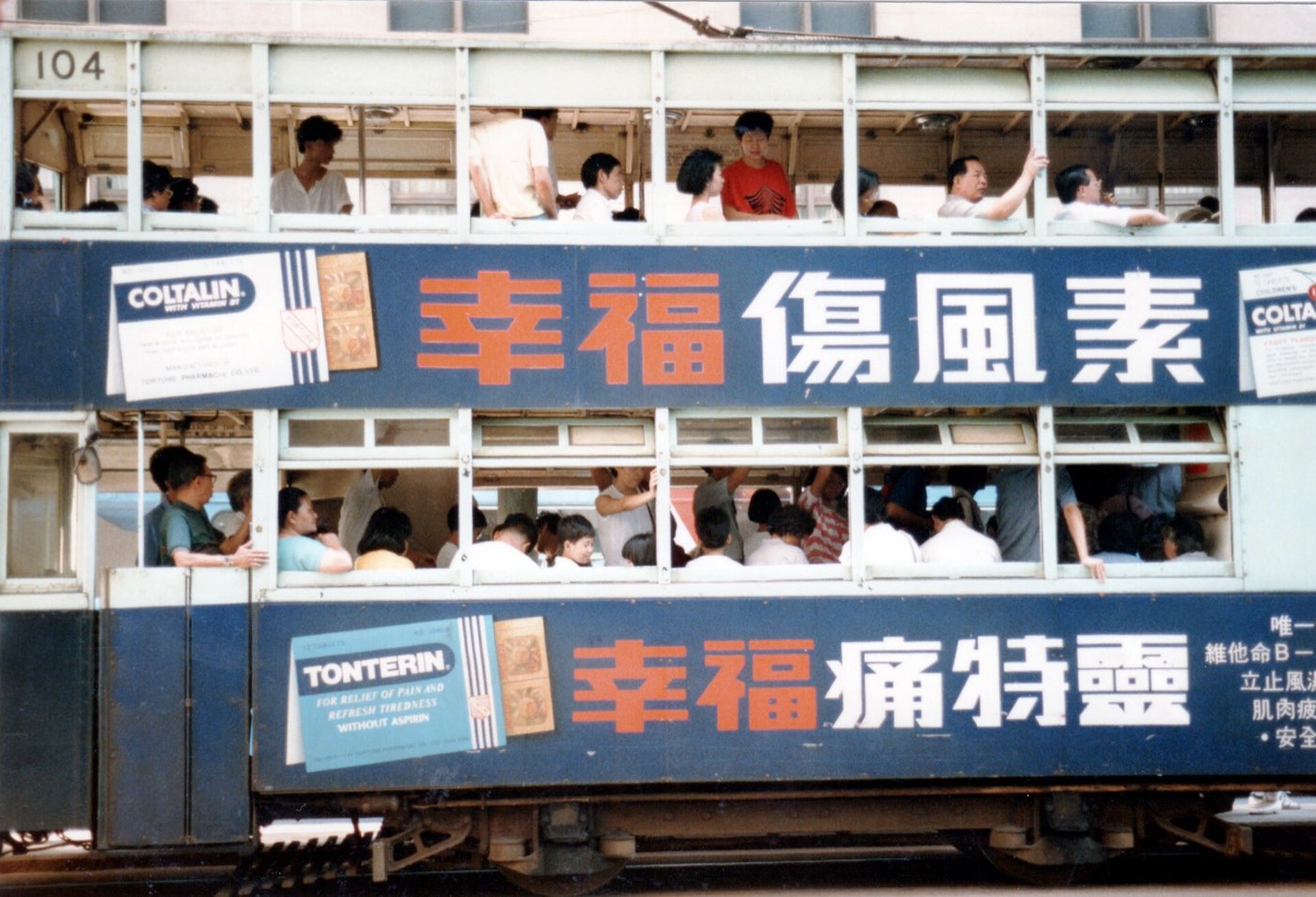 A Hong Kong tram in 1986, packed with passengers, its side painted with a cold-medicine advert in large Chinese characters